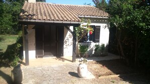 A small house with a tiled roof, a covered porch, and a garden area with a large pot and a small tree. - MAISONETTE T2 30 M2 (Carpentras)