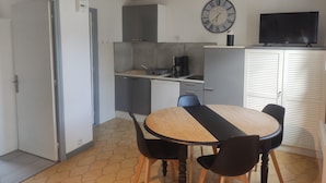 A compact kitchen with a dining area, a clock, and a television. - MAISONETTE T2 30 M2 (Carpentras)