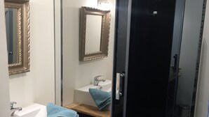 A bathroom with a glass shower enclosure, a sink with a mirror, and a vanity with drawers.