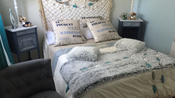 A bedroom with a bed, a grey armchair, and bedside tables with lamps.