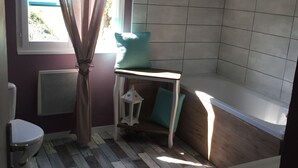 A room with a sloped ceiling, a window with curtains, a wooden wall, and a white chair.