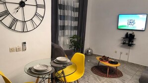 Ein modernes Wohnzimmer mit einem runden Tisch, gelben Stühlen, einer Uhr, einem Fernseher und einem kleinen Couchtisch.