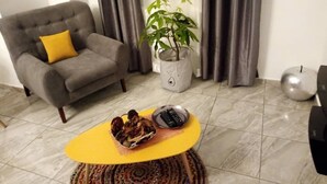 Ein Wohnzimmer mit einem grauen Sofa, einem gelben Couchtisch, einer Topfpflanze und einem kleinen Tisch mit einer Fernbedienung.