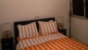 Ein Hotelzimmer mit Bett, Nachttischen, einer Deckenleuchte, einer Klimaanlage und einem Fenster.