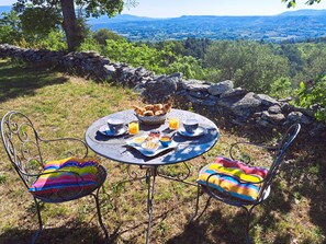 A round table with a stone wall backdrop, two metal chairs with colorful cushions, and a breakfast spread including bread, eggs, and orange juice. - Cante Grillet in Provence at the foot of the Luberon LACOSTE (84480) Chambre FLORY (LACOSTE)