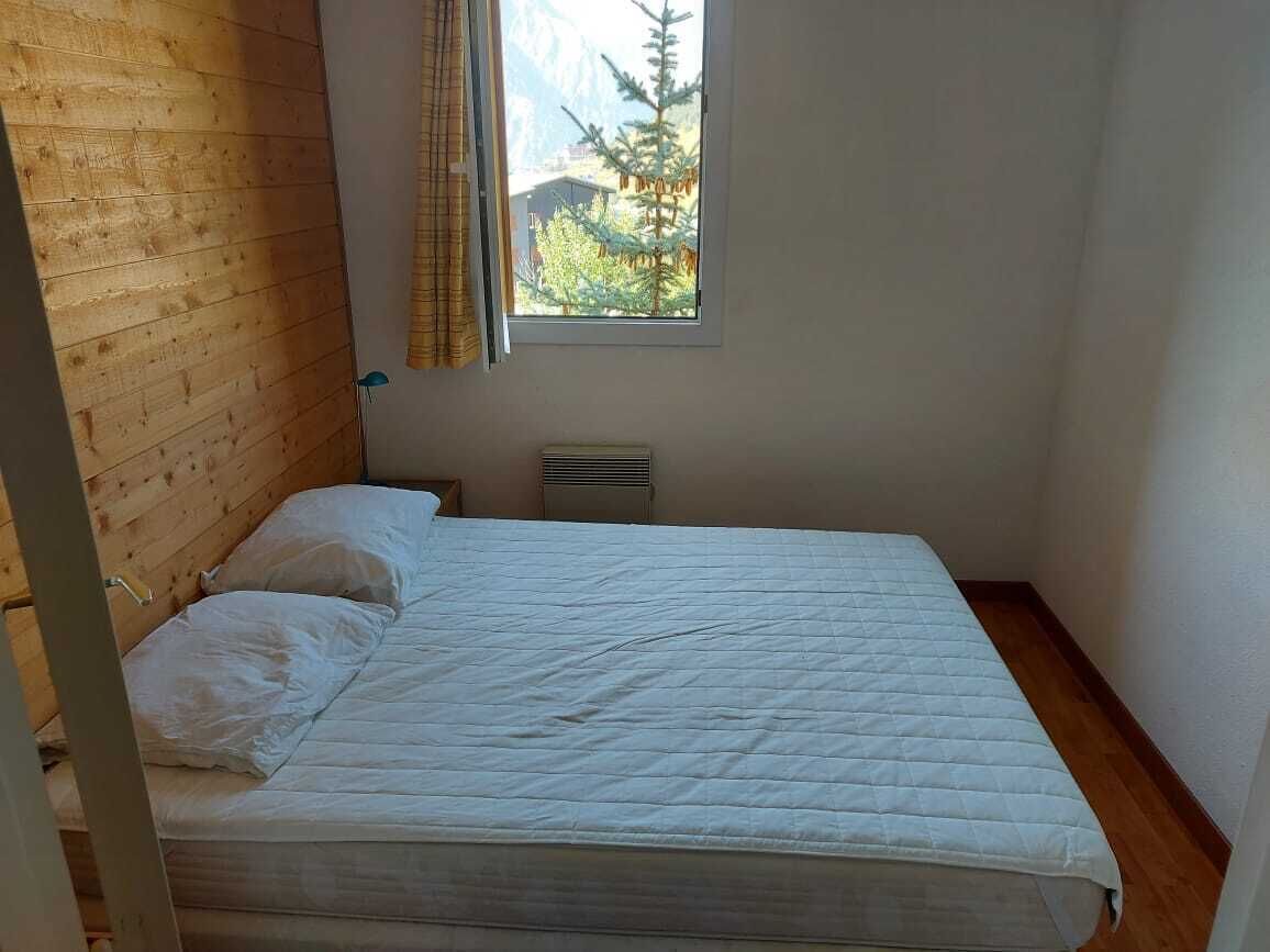 A bedroom with a wooden headboard, a single bed with white bedding, a window with curtains, and a radiator on the wall.