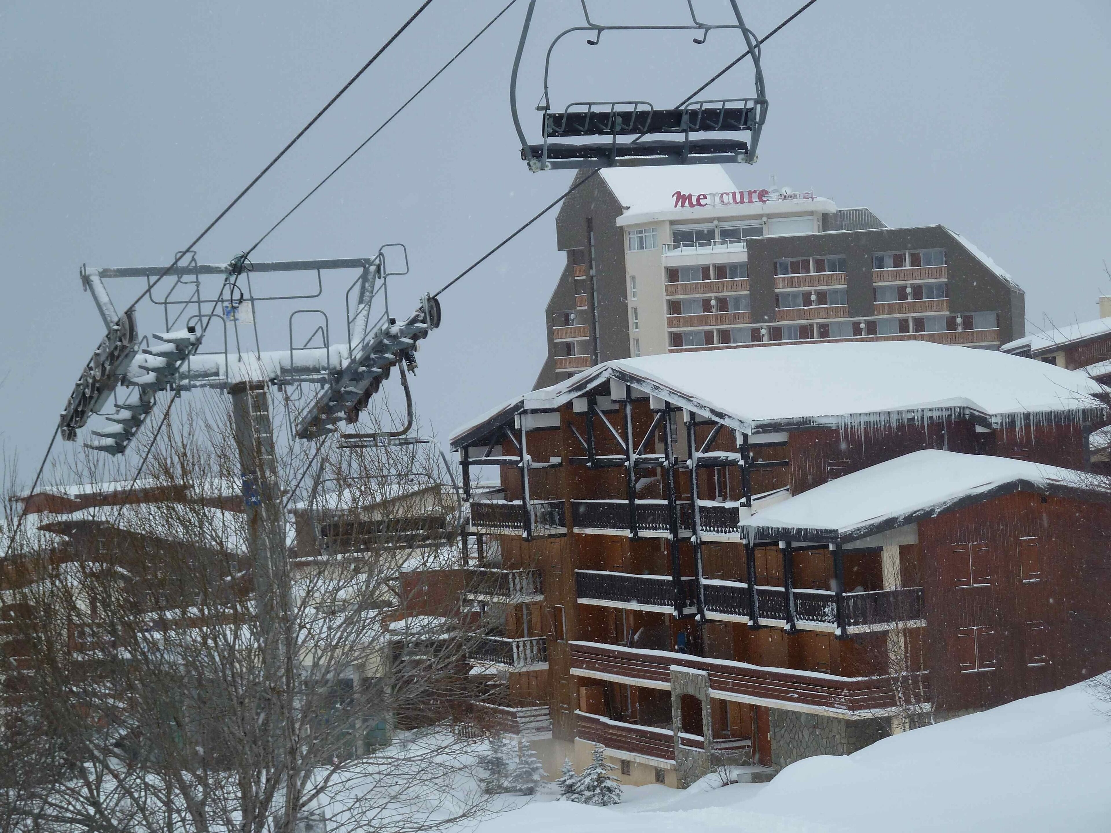 Un télésiège, un bâtiment en bois doté de balcons et une enseigne indiquant « Hôtel Mercure ».