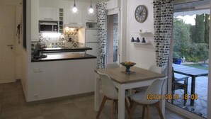A compact kitchen with a dining area, a clock on the wall, and a view of the outdoors through a glass door. - 3P RDJ air-conditioned apartment in residence with swimming pool and tennis court in St Aygulf (Unknown)