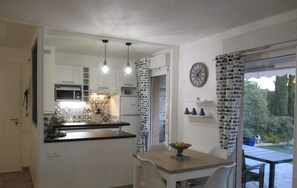 Uma cozinha compacta com área de refeições, um relógio na parede e vista para o exterior através de uma porta de vidro.