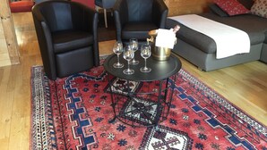 A cozy living area with two black leather chairs, a small round table with wine glasses, a decorative rug, and a grey sofa with a white throw blanket. - CHALET SABOT OF STANDING VENUS AT THE FOOT OF TRACKS (Fontcouverte-la-Toussuire)