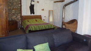 A bedroom with a bed, a wooden wardrobe, a stone wall, a mirror, and a large window. - Village house at the foot of Mont Ventoux (Bédoin)