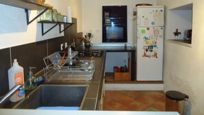 A compact kitchen with a sink, stove, and refrigerator, featuring a window above the oven and a shelf above the sink. - Village house at the foot of Mont Ventoux (Bédoin)