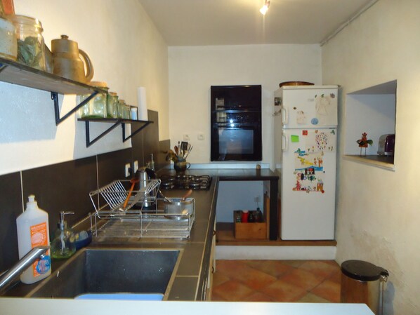 A compact kitchen with a sink, stove, and refrigerator, featuring a window above the oven and a shelf above the sink.