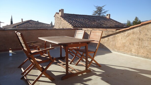 A wooden table and chairs on a rooftop terrace with a view of buildings and trees. - Village house at the foot of Mont Ventoux (Bédoin)