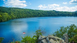 Un lago con un bote, rodeado de bosque denso y terreno rocoso.