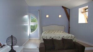 Un dormitorio con cama, mesita de noche, lámpara, ventana y vista a follaje exterior.