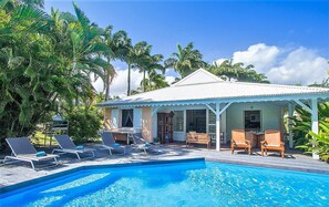 A poolside area with lounge chairs and a small building with a white roof. - Creole villa with sea view and private pool between Ste Rose and Deshaies (SAINTE ROSE)