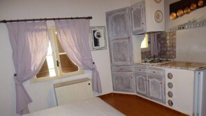 A bedroom with a bed, a window with curtains, a radiator, and a kitchenette with cabinets and a stove. - CARQUEIRANNE APARTMENT WITH POOL 2MN BEACH (Carqueiranne)