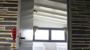 A doorway leading to a bedroom with two beds, a window, and a brick wall.