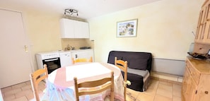 A compact kitchen with white cabinets, a dining table with chairs, and a black sofa.