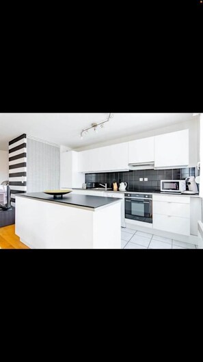 A modern kitchen with white cabinets, a black backsplash, and a central island with a bowl.