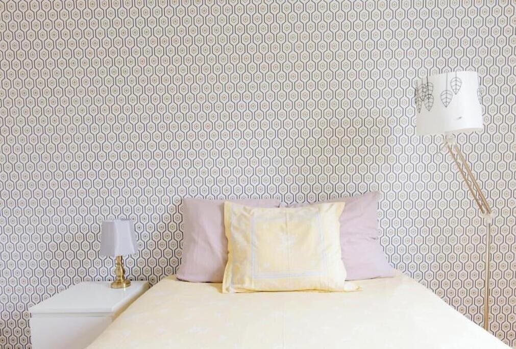 Un lit avec un mur décoré d’un motif, une lampe de chevet et un luminaire fixé au mur.