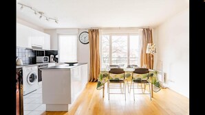 Eine moderne Küche mit Kochinsel, Essbereich mit Tisch und Stühlen sowie ein großes Fenster mit Vorhängen.