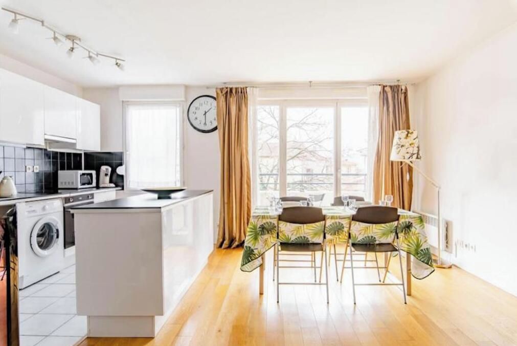 Una cocina moderna con una isla central, una zona de comedor con mesa y sillas, y un ventanal con cortinas.