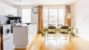 Une cuisine moderne dotée d’un îlot central, d’un coin repas avec une table et des chaises, et d’une grande fenêtre agrémentée de rideaux.