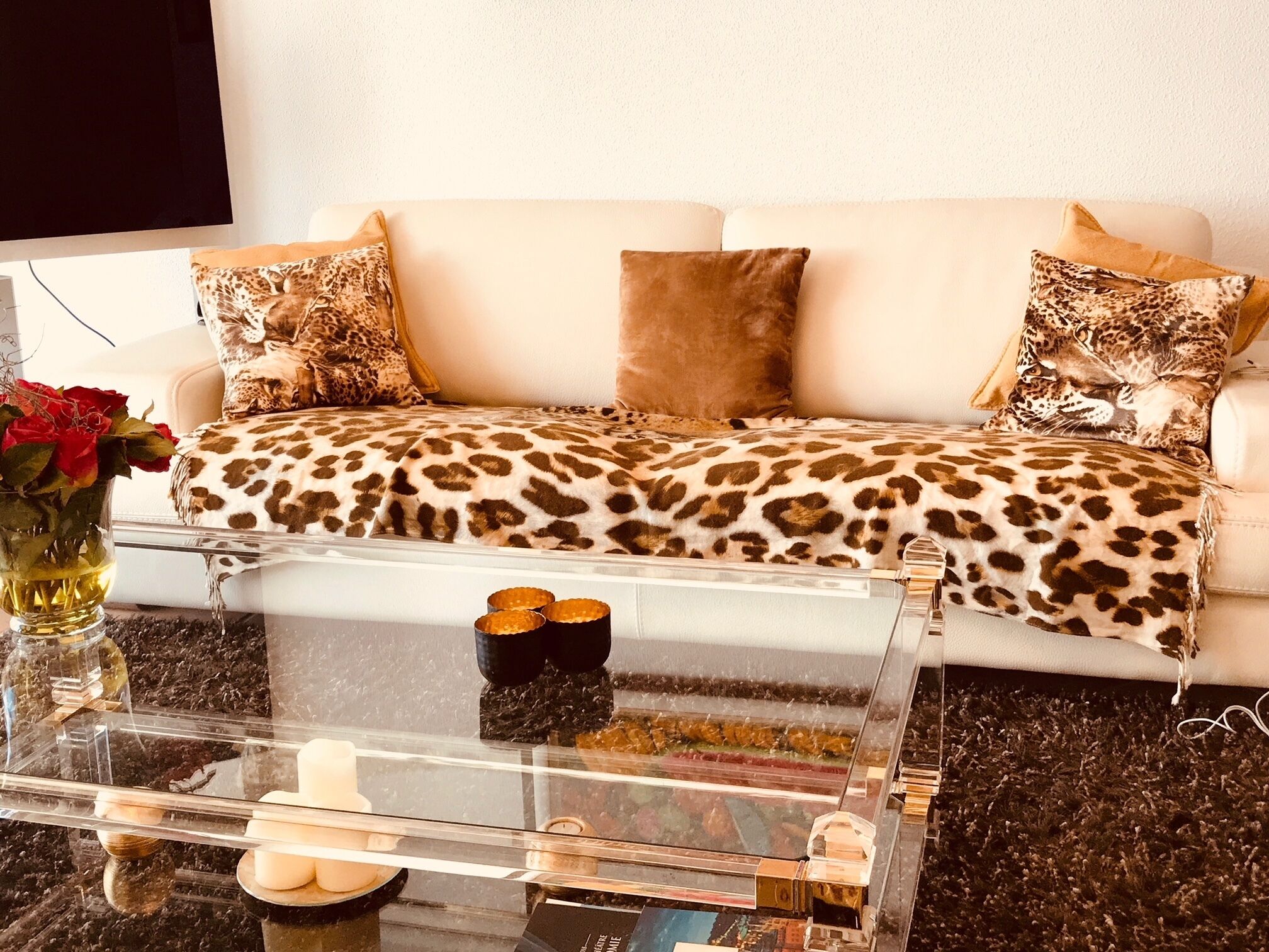 Ein Wohnzimmer mit einer Couch, die mit Leopardenmuster bezogen ist, einem Glastisch mit dekorativen Gegenständen und einer Vase mit roten Rosen.