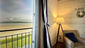 En balkong med utsikt över stranden, en lampa och en randig fåtölj.