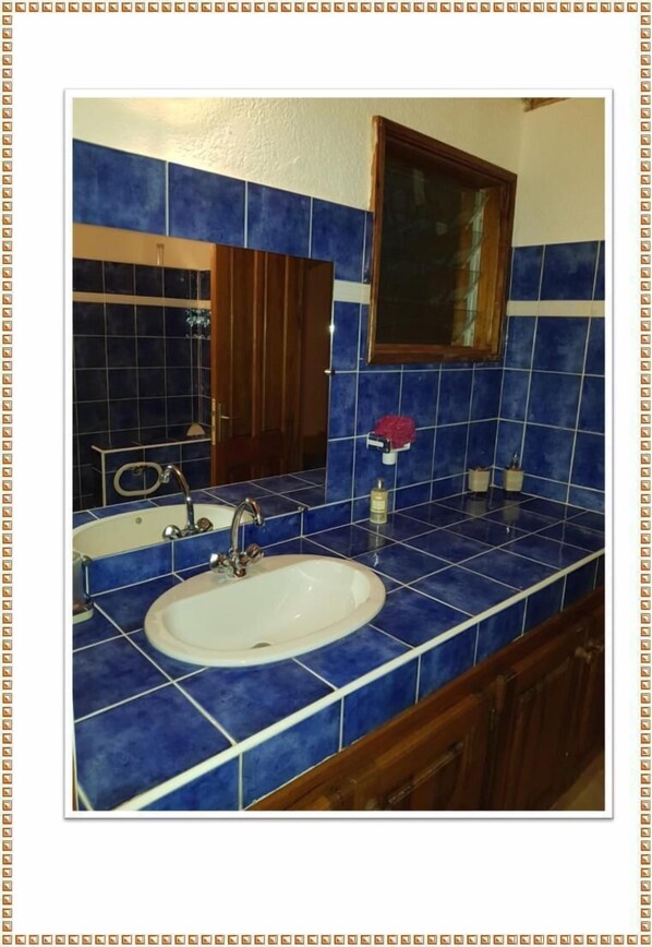 Bathroom features a white sink, mirror, and blue-tiled walls, along with a wooden cabinet and a decorative flower.