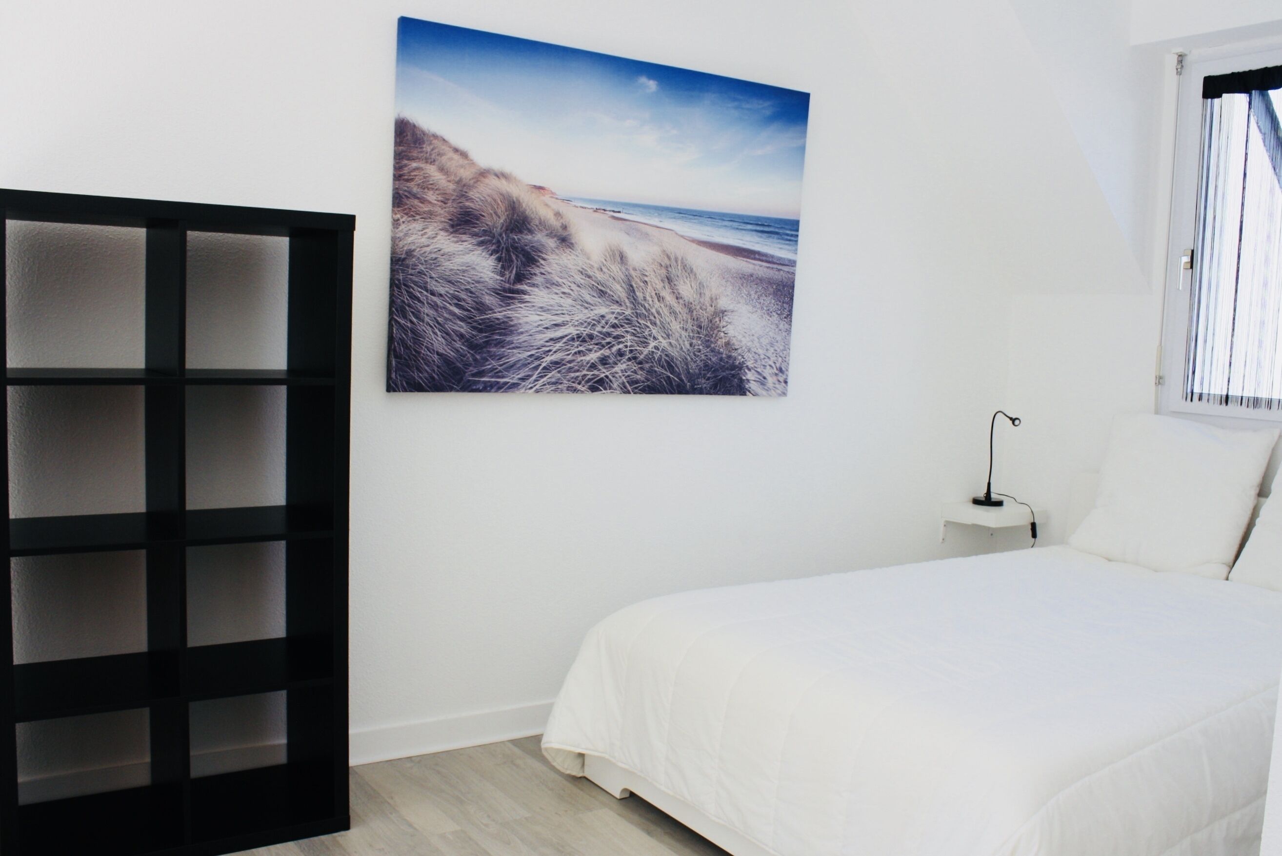 Ein Schlafzimmer mit einem Bett, einem Wandregal und einem Strandbild.