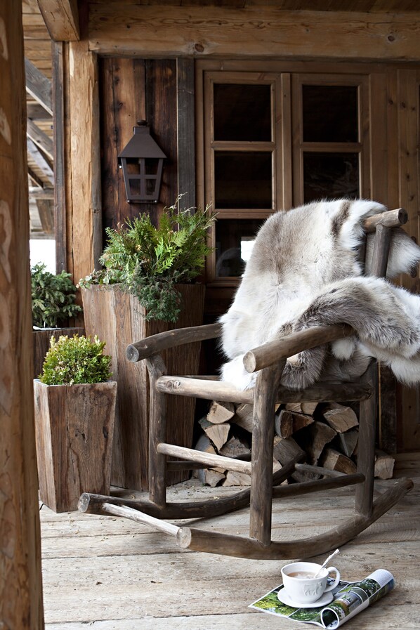 A rustic wooden rocking chair with a white furry object on it, a wooden door, and a lantern in the background.