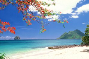 A beach with clear turquoise water, white sand, and a distant mountain. - Le 222***, superb Duplex T4, residence with swimming pool, beach and restaurants 500m away (Le Diamant)