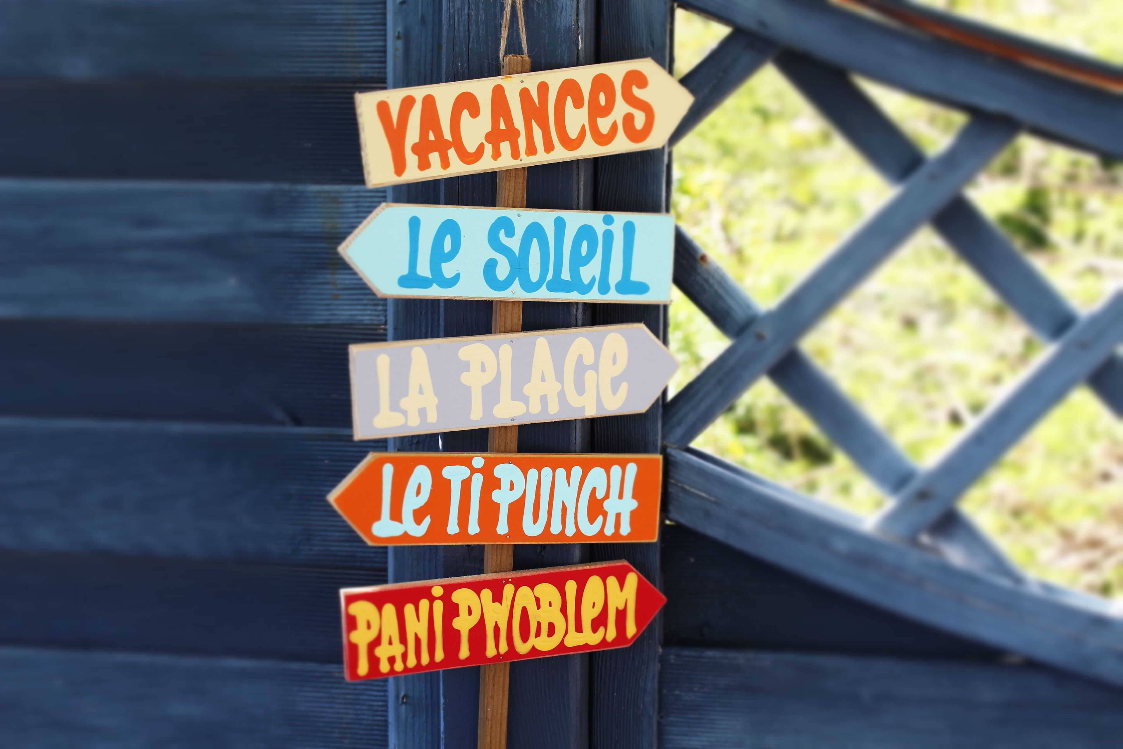 A sign with multiple directional arrows, each labeled with different destinations such as "Vacances," "Le soleil," "La plage," "Le ti punch," and "Pani problem."