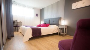Ein Schlafzimmer mit einem Bett, einem Nachttisch, einem Sessel und einem Fenster mit Vorhängen.