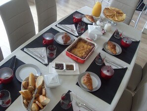 Ein Frühstückstisch ist gedeckt mit Croissants, Brot, einem Obstkuchen und einer roten Kaffeekanne.