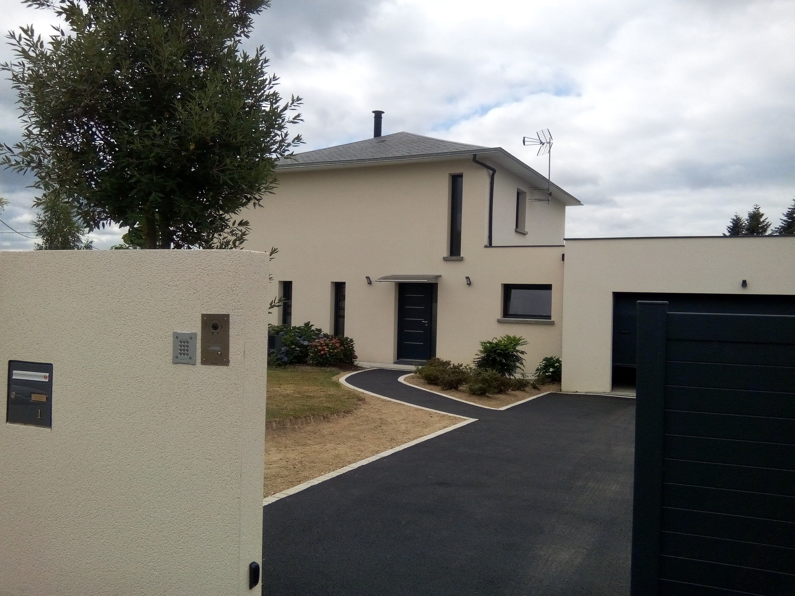 Un bâtiment moderne à deux étages, doté d’un toit plat, d’un portail noir et d’une allée pavée menant à l’entrée.