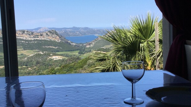 Une table avec deux verres à vin et une assiette, donnant sur un paysage montagneux avec un lac.