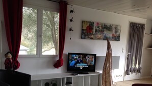Un salon avec un téléviseur, des meubles blancs, un rideau rouge et un tableau accroché au mur.