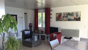 Un salon comprenant un coin repas, un téléviseur et une grande fenêtre ornée de rideaux rouges.