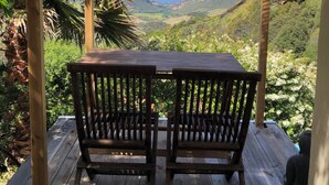 Une terrasse en bois avec deux chaises, donnant sur un paysage pittoresque d’une vallée et de montagnes.