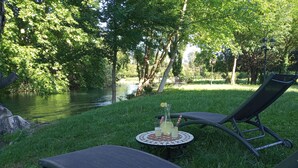 Un espace extérieur paisible, aménagé avec deux fauteuils confortables et une petite table, le tout mis en valeur par un décor de verdure luxuriante et un plan d'eau tranquille.