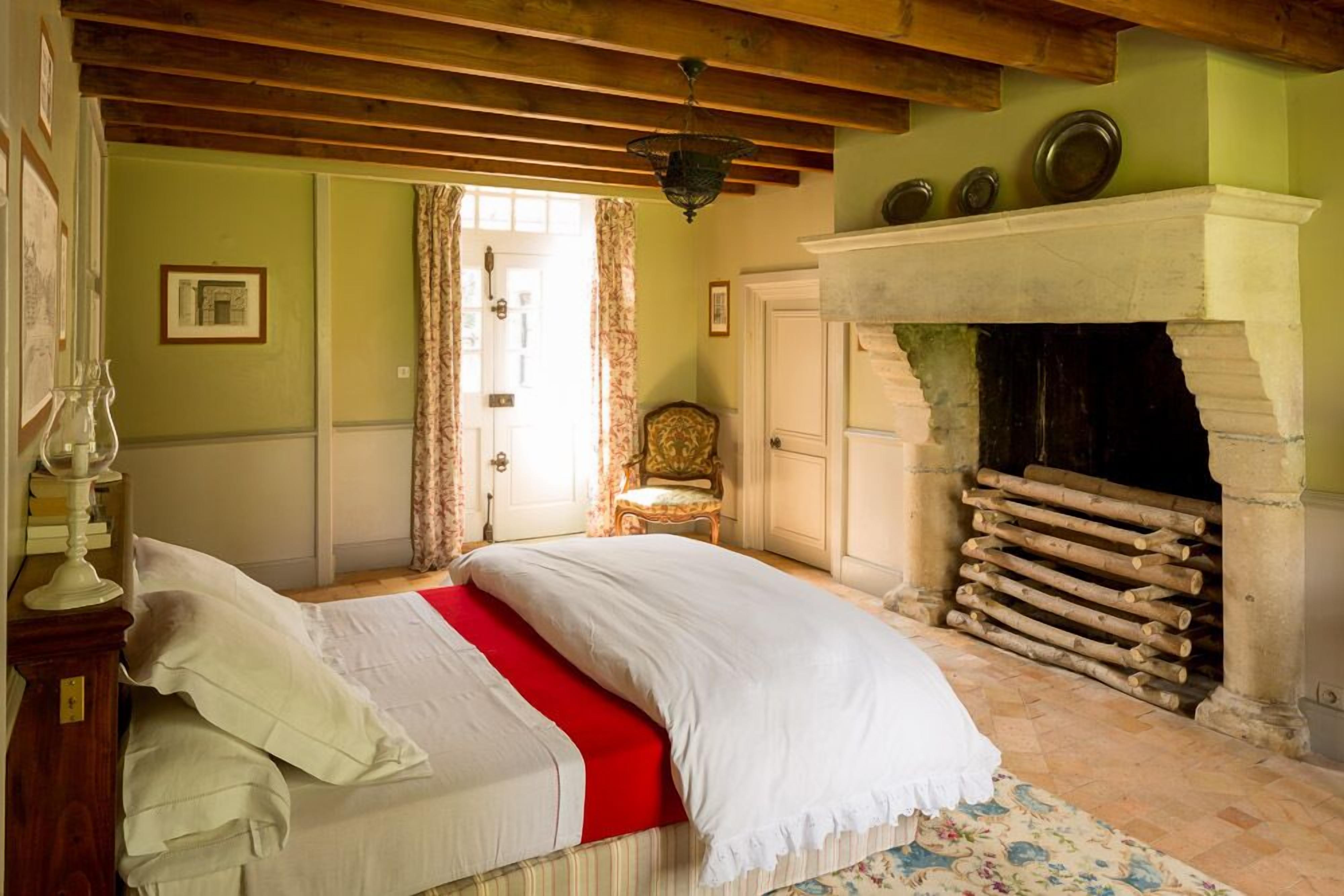 A bedroom with a bed, a fireplace, a chair, and a door.