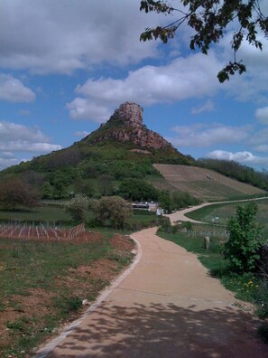 Un sentier pavé mène à un sommet de colline rocheuse, entouré de verdure et surplombé d’un ciel dégagé.