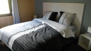 Een net opgemaakt bed met gestreept beddengoed, een houten hoofdbord en een nachtkastje met een lamp.