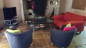 Een woonkamer met een stenen open haard, een rode bank, twee fauteuils en een televisie op een meubel.