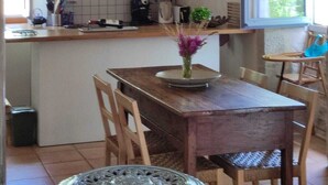 Een landelijke keuken met zichtbare houten balken, een houten eettafel en een raam met uitzicht op groen.