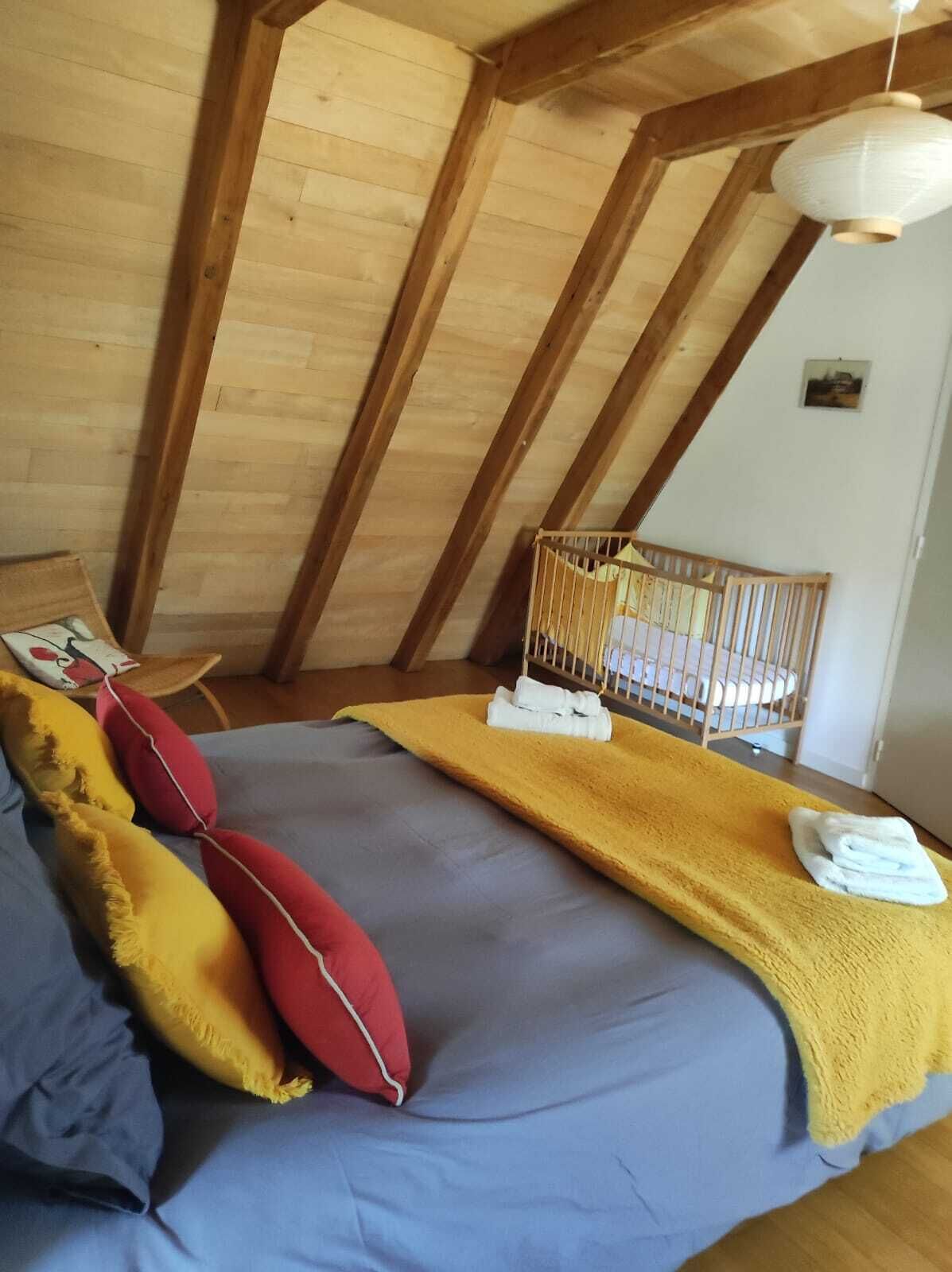 Una habitación acogedora con cama, almohadas, una cuna y una lámpara colgante.